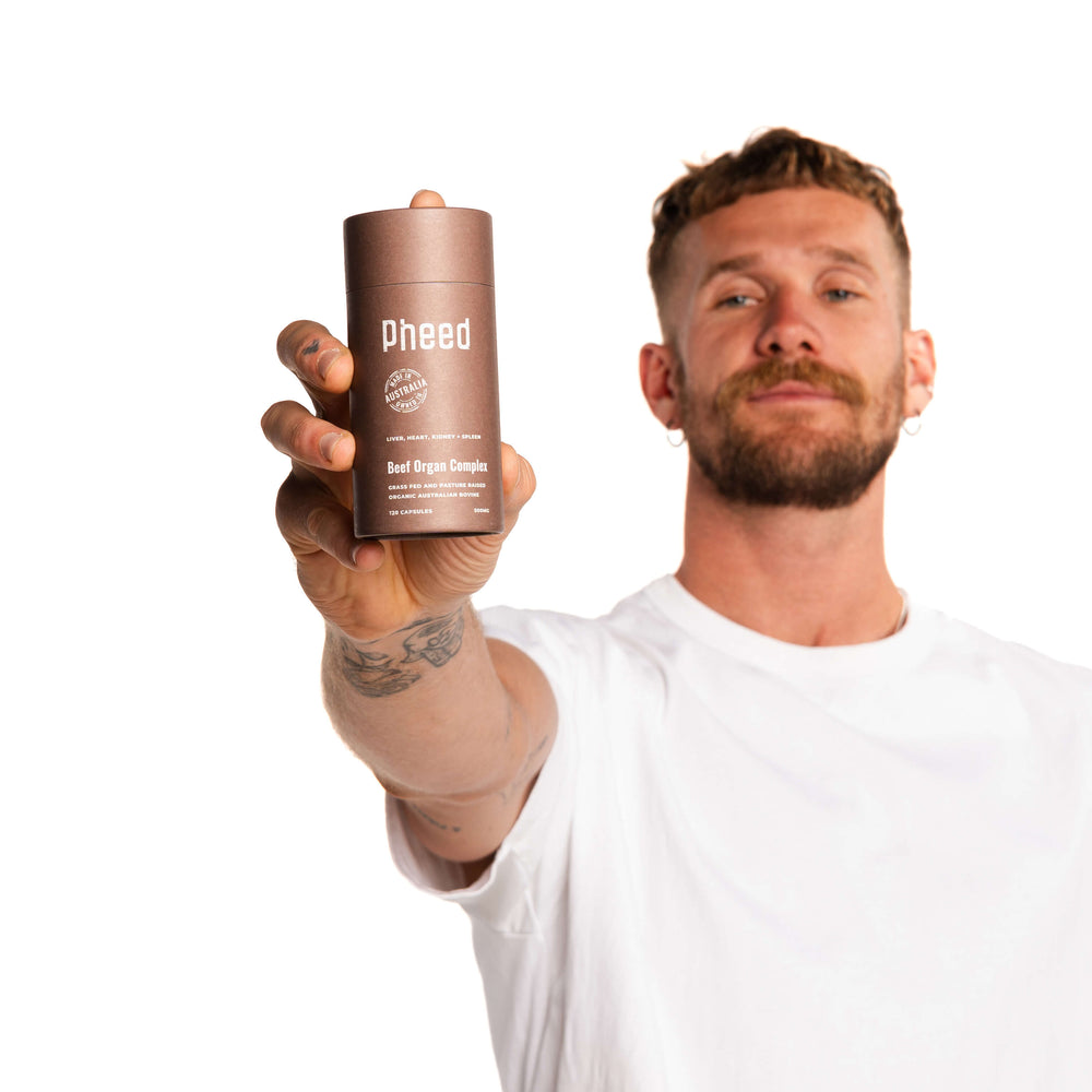 Man holding a brown bottle labeled 'Pheed' against a white background. Contains beef liver, beef kidney, beef heart and beef spleen freeze-dried powder in capsules.