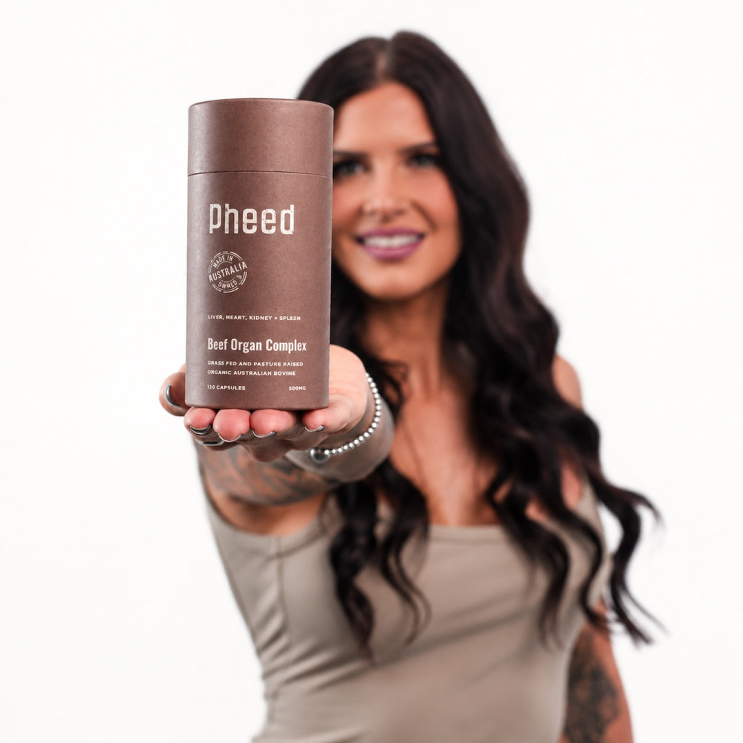 Woman presenting Pheed Beef Organ Complex capsules toward the camera.