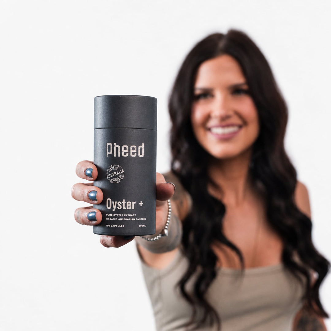Woman smiling while holding a Pheed Oyster+ capsule bottle towards the camera.
