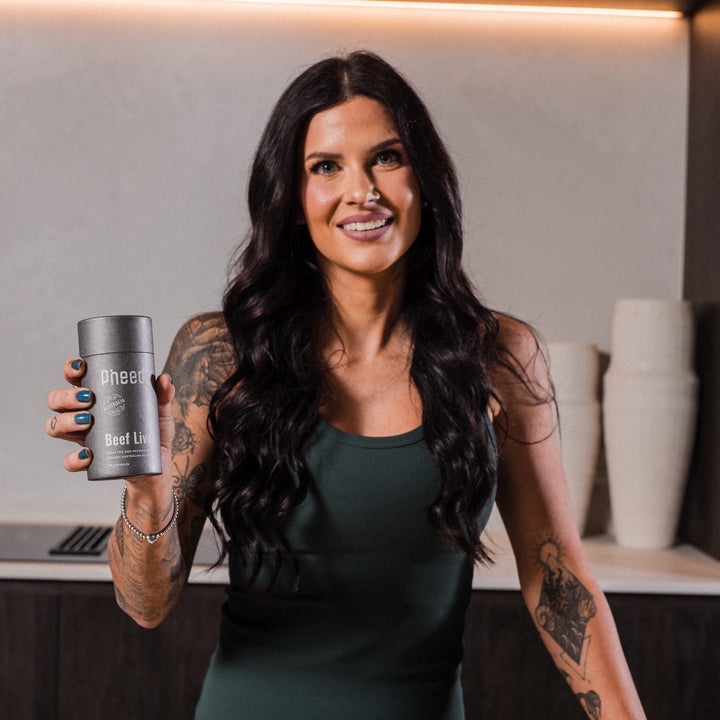 Woman holding Pheed Beef Liver Capsules 120-capsule bottle in a modern kitchen.