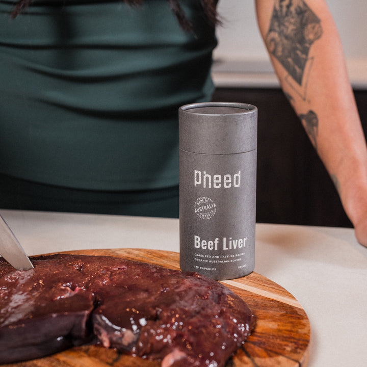 Pheed Beef Liver Capsules 120-capsule bottle beside fresh beef liver on a chopping board.
