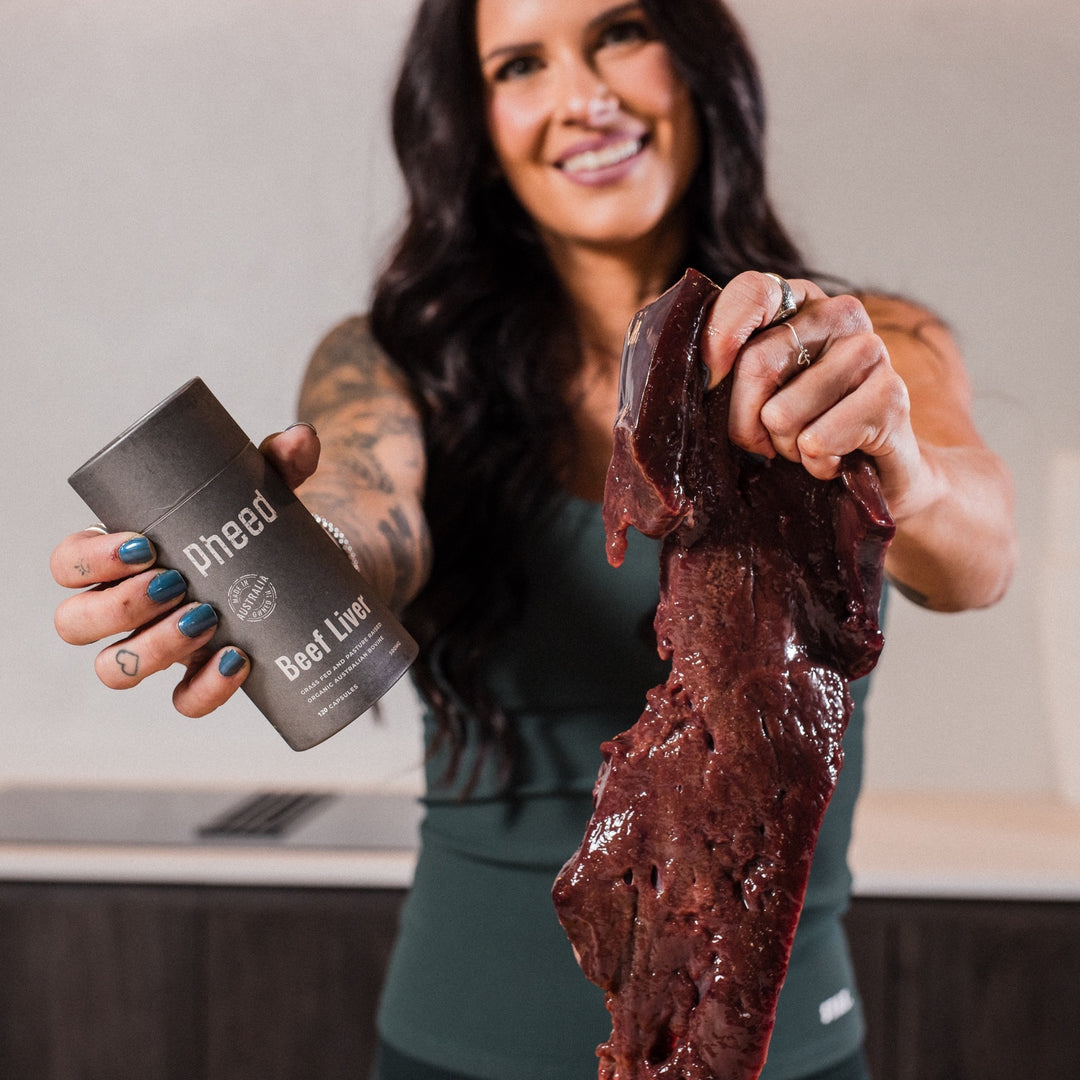 Woman holding Pheed Beef Liver Capsules and fresh beef liver in a kitchen.
