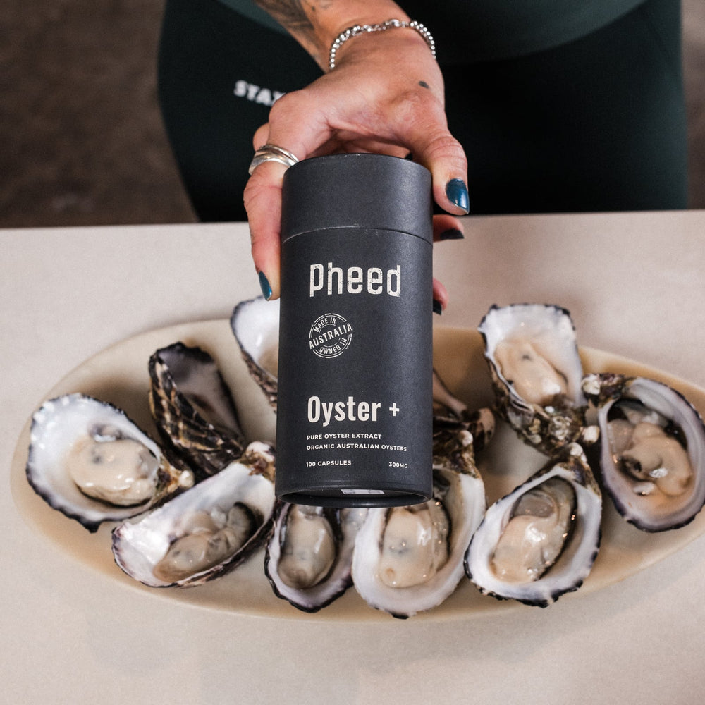Pheed Oyster+ capsule bottle held above a platter of freshly opened oysters.