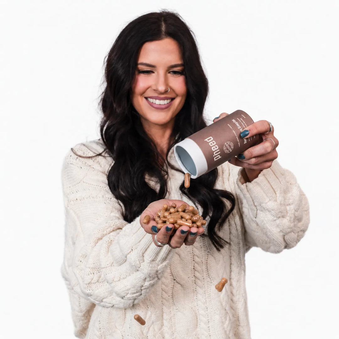 Woman in a cream cardigan pouring Pheed Beef Organ Complex capsules into her hand.
