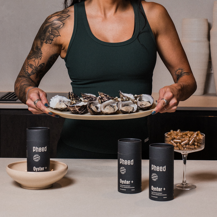 Person holding a plate of oysters with 'Pheed' containers on a table.