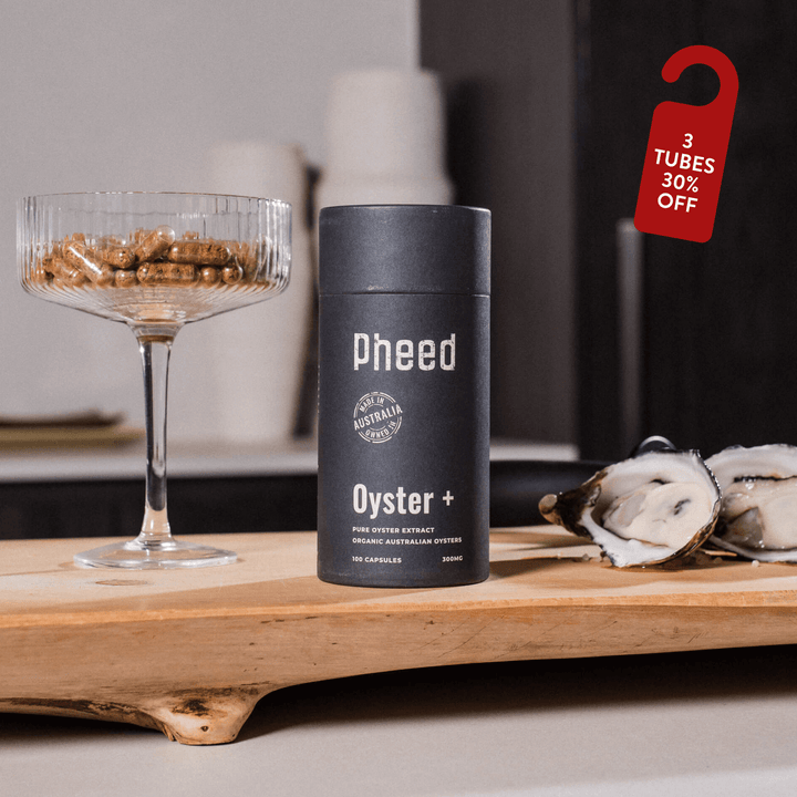 Pheed Oyster+ supplement container on a wooden surface with oysters and a glass in the background.