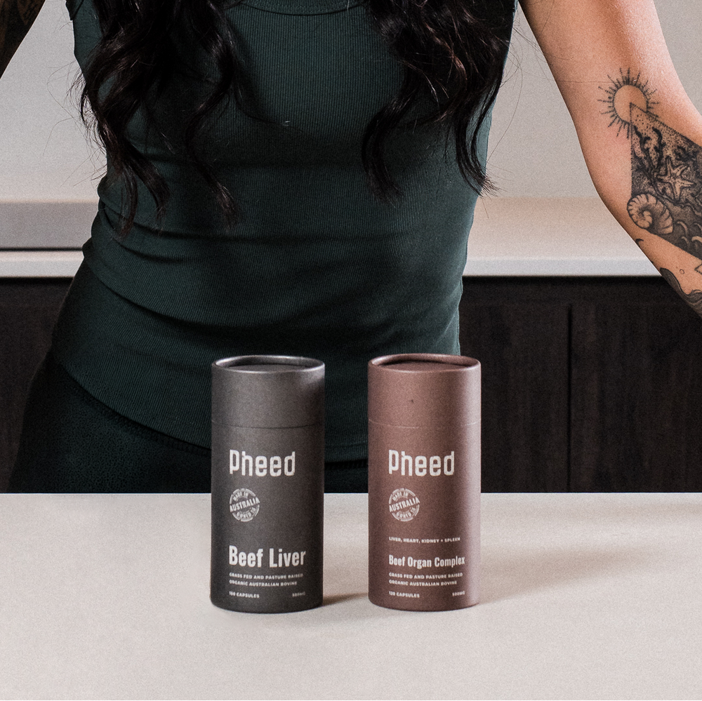 Pheed Beef Liver and Beef Organ capsules product cans on a table with a person wearing a green dress in the background.