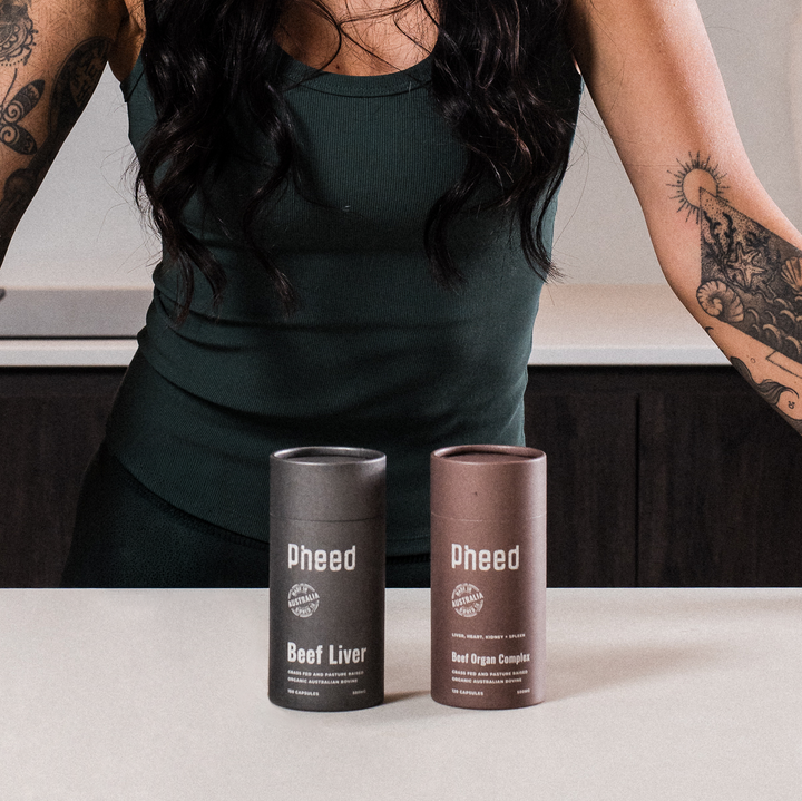 Pheed Beef Liver and Beef Organ capsules product cans on a table with a person wearing a green dress in the background.