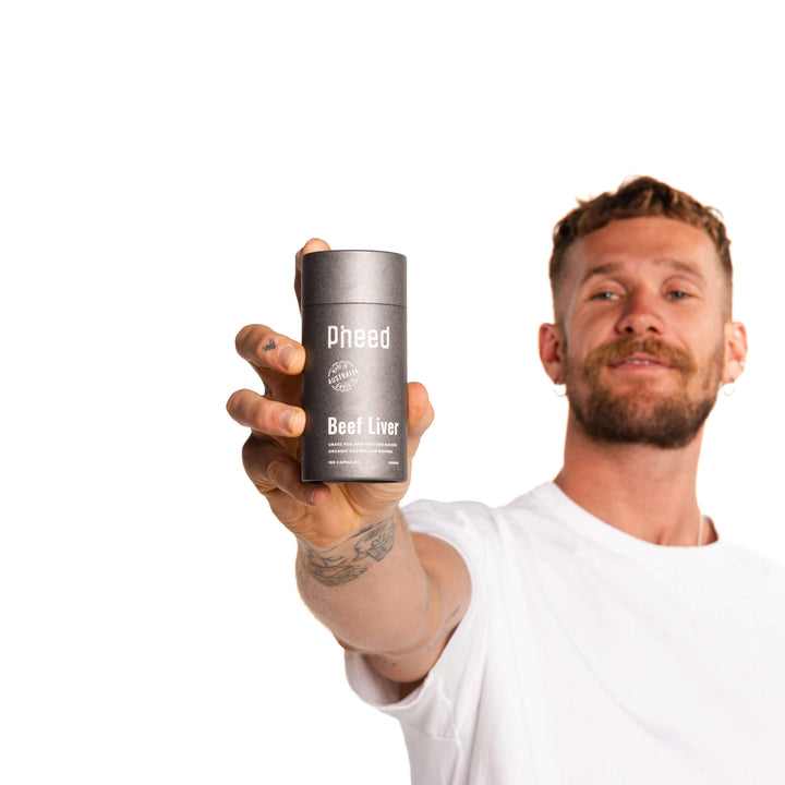 Man holding a supplement container containing beef liver capsules labeled 'Pheed' against a white background