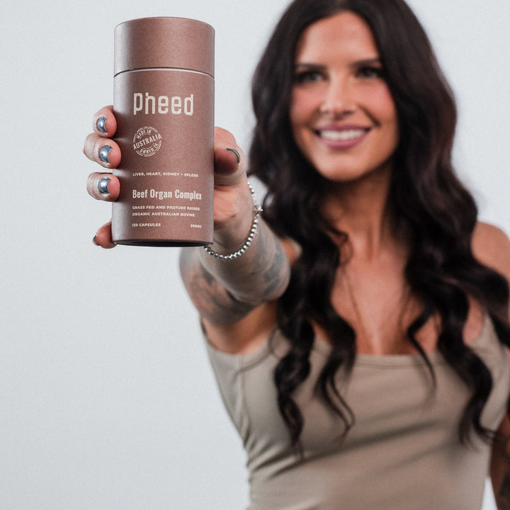 Woman holding a brown supplement container labeled 'pheed' against a plain background
